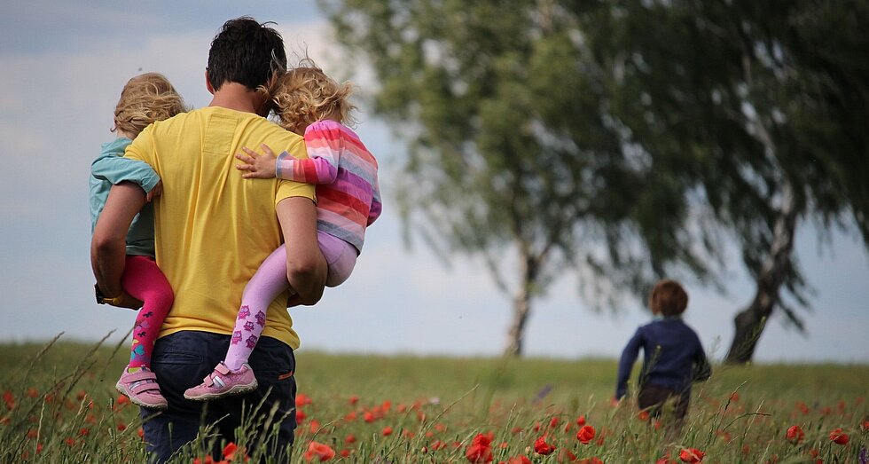 Vater mit seinen beiden Kindergartenkindern auf dem Arm in der Natur