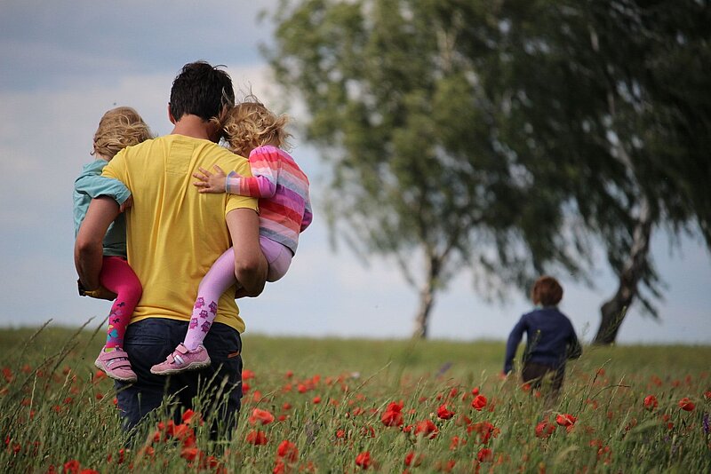 Vater mit seinen beiden Kindergartenkindern auf dem Arm in der Natur