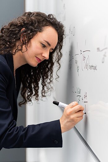 Frau schreibt mit schwarzem Stift auf weißer Wand