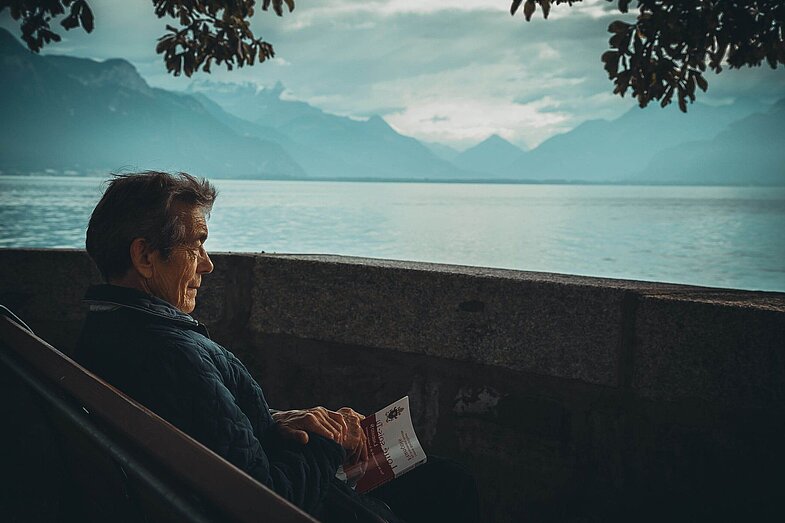 Älterer Man sitzt am See und hat ein Buch in der Hand