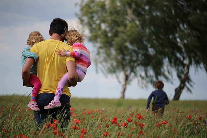 Alleinerziehende Vater mit seinen beiden Kindergartenkindern auf dem Arm in der Natur