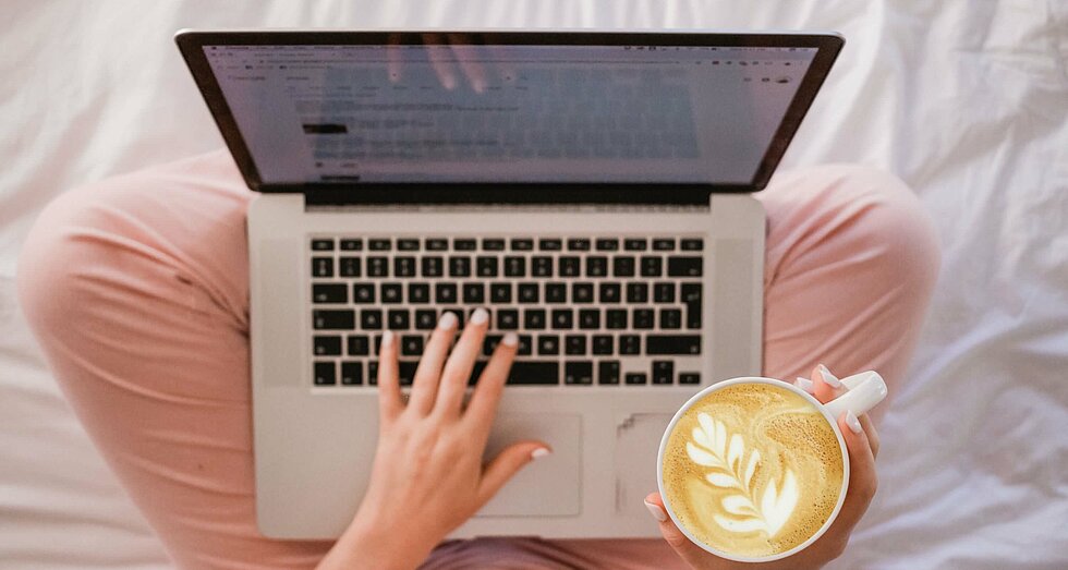 Vogelperspektive auf Person mit Laptop auf dem Schoß im Bett