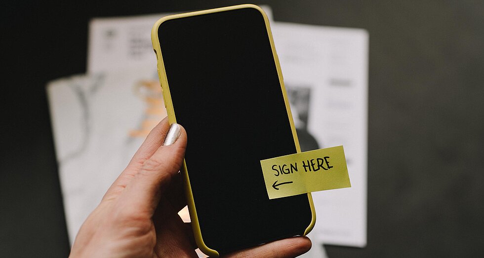 Handy mit gelbem postet "Sign here"