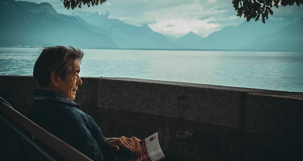 Älterer Man sitzt am See und hat ein Buch in der Hand