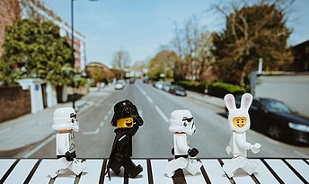Vier Playmobil Figuren in schwarz und weiß laufen wie die Beatles über einen Zebrastreifen