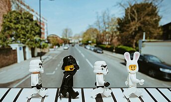 Finanzamt_daniel-cheung-B7N0IjiIJYo-unsplash Vier Playmobil Figuren in schwarz und weiß laufen wie die Beatles über einen Zebrastreifen