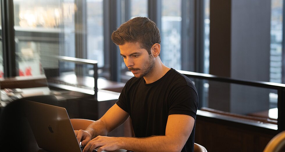 Mann in schwarzem T-Short beim Arbeiten am Laptop