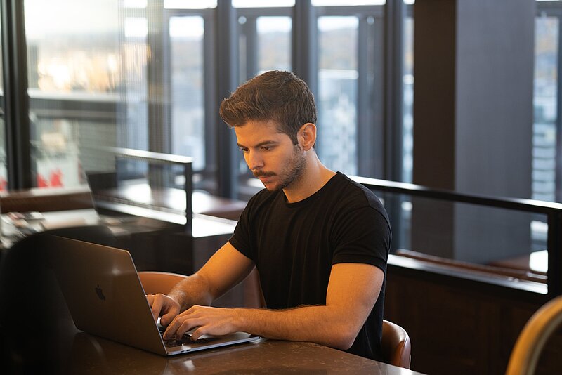 Gewerbesteuererklärung-Anthony Riera-Unsplash Mann in schwarzem T-Short beim Arbeiten am Laptop