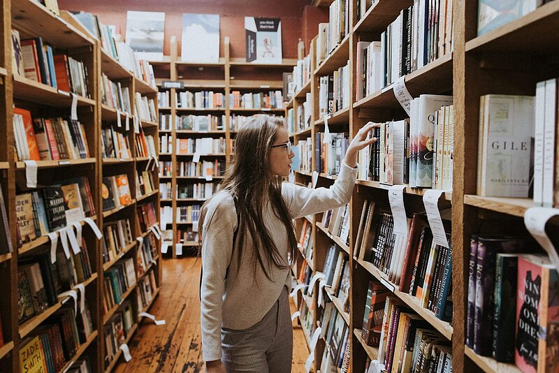 Ausbildungsfreibetrag Junge gebildete Frau an einem Bücherregal in der Bibliothek