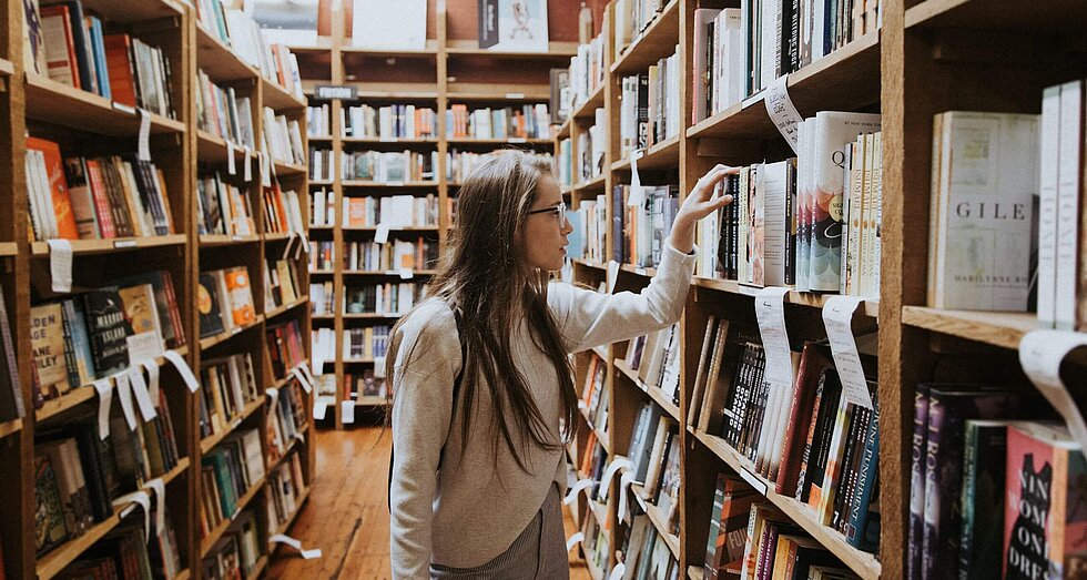 Junge gebildete Frau an einem Bücherregal in der Bibliothek