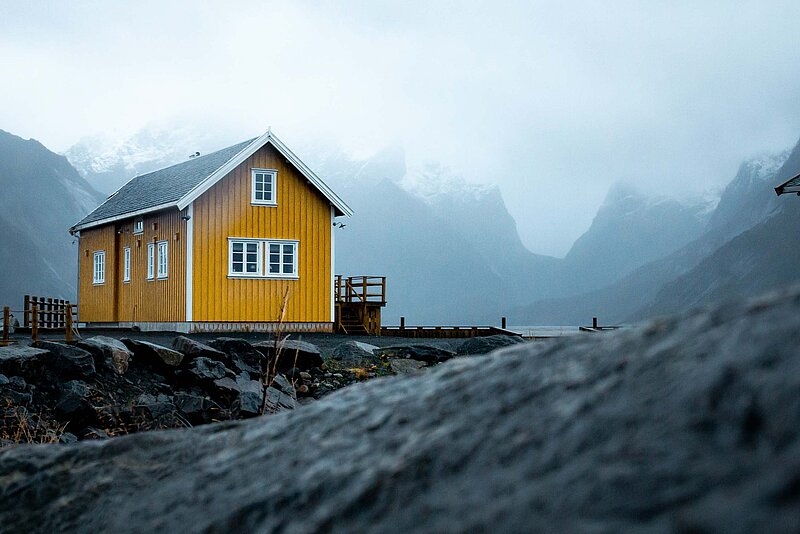Vermietung und Verpachtung Steuer- Hans M-Unsplash. Gelbes Holzhaus in grauen Bergen mit Nebel und Wolken