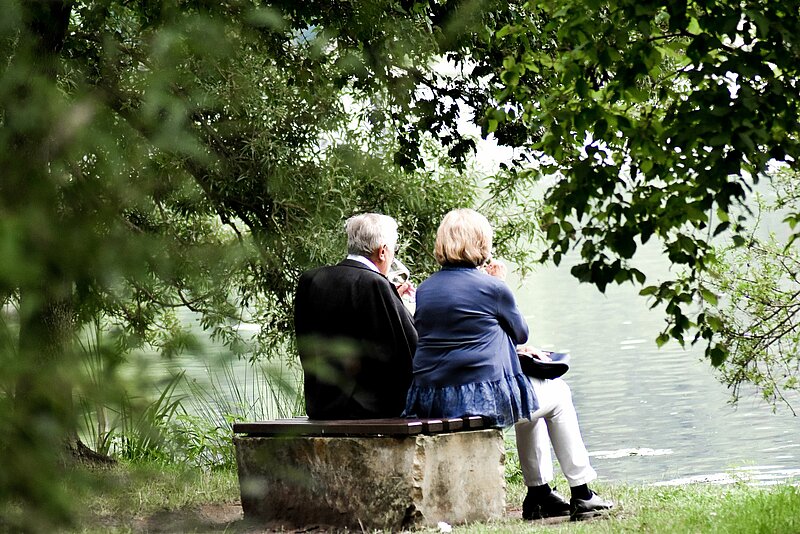 Altes Ehepaar genießt auf einem Baumstumpf sitzend den Blick in die grüne Natur