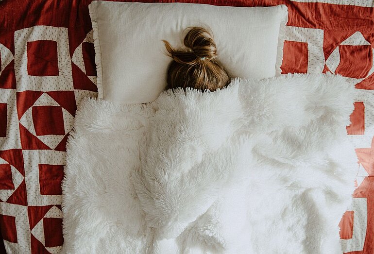 Krankheitskosten absetzen- Kelly Sikkema-Unsplash. Frau in Bett, Decke über den Kopf gezogen