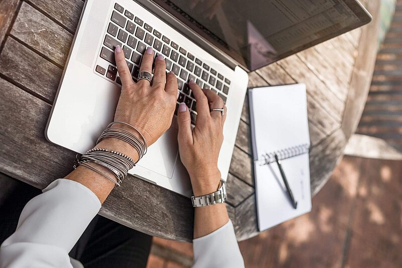 Rentner_Steuer_linkedin-sales-navigator-unsplash Hände auf Laptop Tastatur, der Laptop steht auf einem Holztisch im Garten