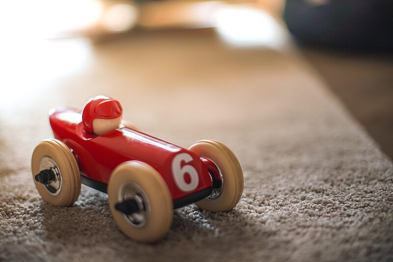 Artem Beliaikin via Unsplash Spielzeugauto aus Holz auf Teppich