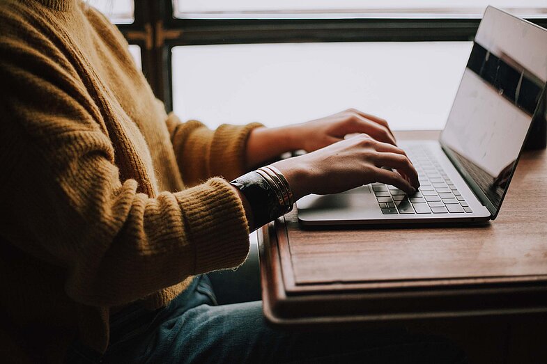 Person sitzt am Schreibtisch und arbeitet an einem Laptop