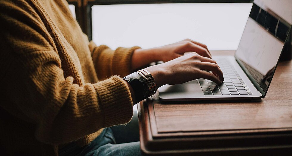 Person sitzt am Schreibtisch und arbeitet an einem Laptop