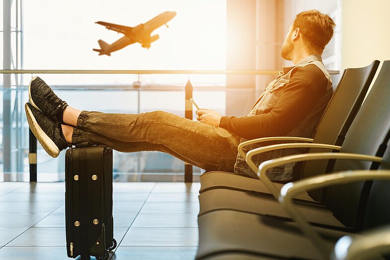 Junger Businesshengst auf Dienstreise am Flughafen mit Blick auf ein abhebendes Flugzeug