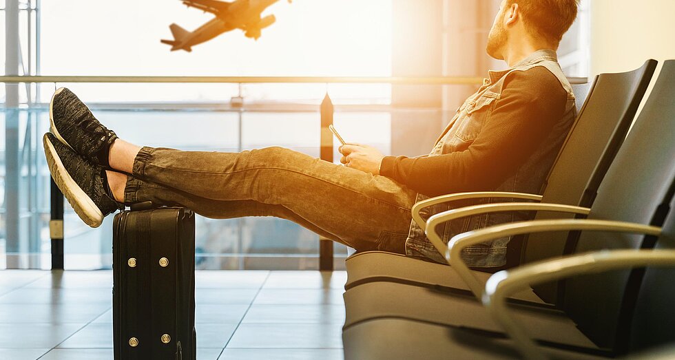 Reisekosten von der Steuer absetzen Junger Businesshengst auf Dienstreise am Flughafen mit Blick auf ein abhebendes Flugzeug