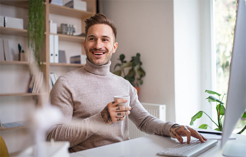 Steuertipps_AdobeStock_318589338.jpeg Junger Mann sitzt gut gelaunt am Schreibtisch