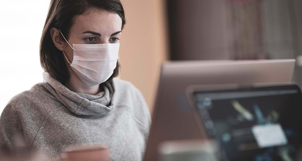 Frau mit Atemmaske vor Laptop