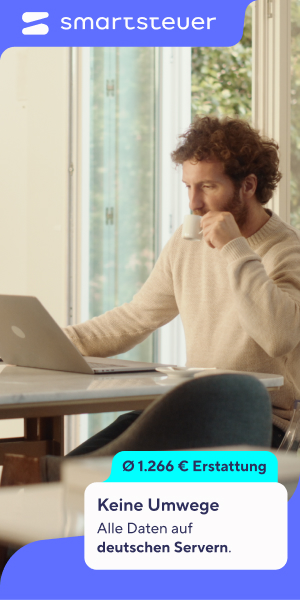 Mann sitzt am Küchentisch vor Laptop und telefoniert.
